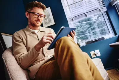 Male with glasses looking sitting on a sofa seat looking at his tablet