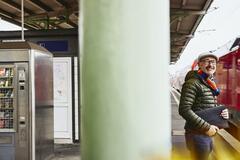 Man holding a laptop case/bag standing on a train platform.