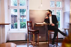 male sitting at table with a coffee, smiling looking away.
