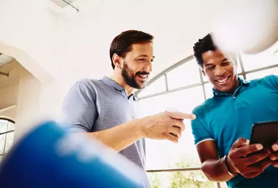 Two smiling colleagues (men) looking at a phone.
